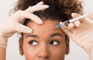 Young woman getting botox injection in center of forehead. 